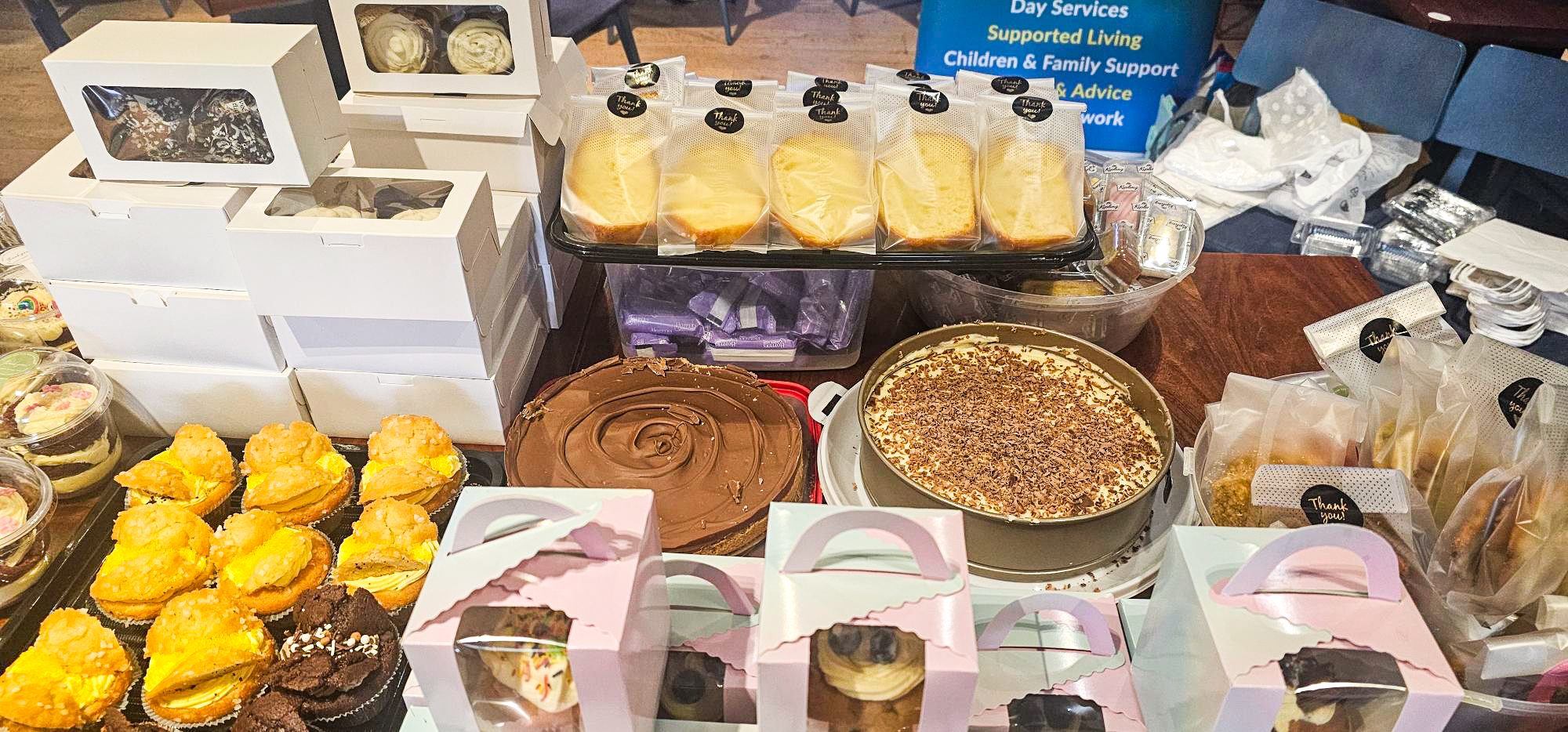 Many different cakes arranged across a table, for sale