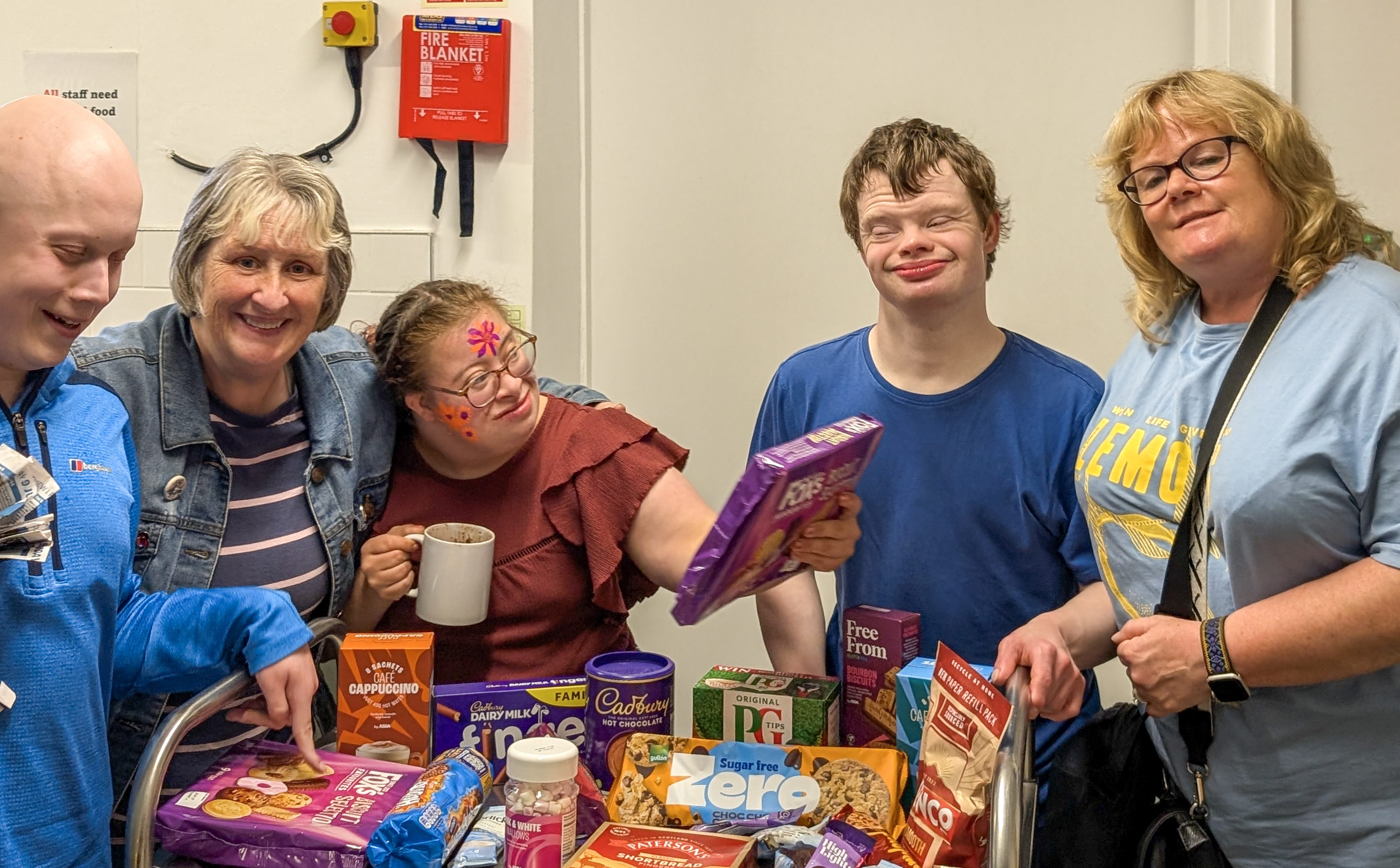 Five smiling people standing around a trolley filled with different packs of biscuits, which they have won